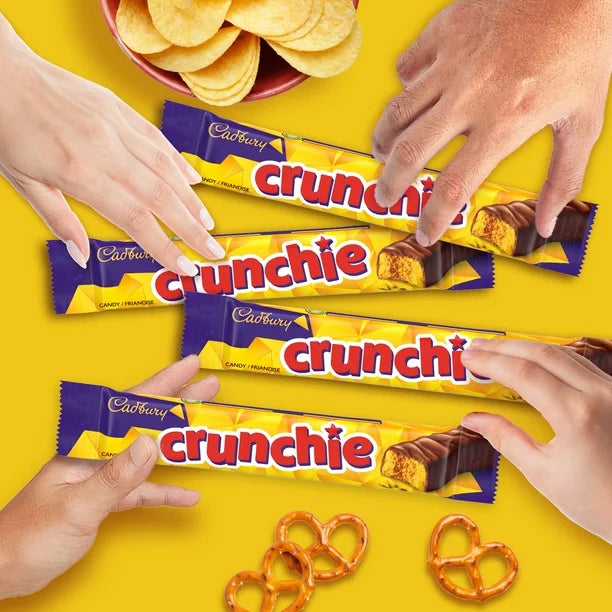 Cadbury Crunchie chocolate bars with hands reaching for them on a yellow background