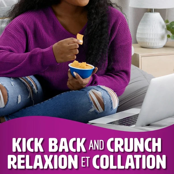 Person in purple sweater and ripped jeans sitting on a couch with a laptop, eating chips from a blue bowl.